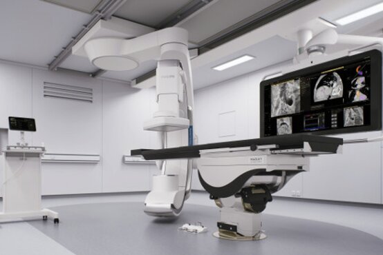 Moderner Hybrid-OP-Saal mit roboter-assistiertem Operationstisch, großem C-Bogen-Röntgengerät, Monitor mit CT-Aufnahmen und fahrbarem Gerätewagen