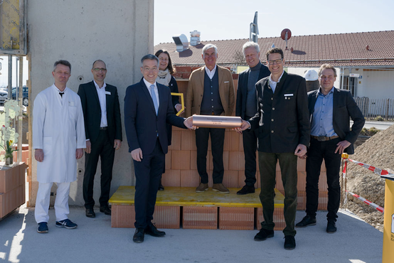 Acht Erwachsene in Businesskleidung bei Grundsteinlegung zum Ronald McDonald Haus in Vogtareuth