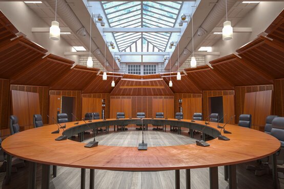 Moderner Konferenzsaal mit ovalem Holztisch, Ledersesseln und Mikrofonen