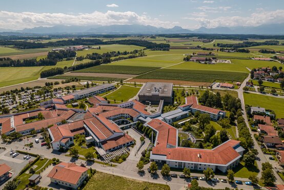 Luftaufnahme der Schön Klinik Vogtareuth mit roten Ziegeldächern, grünen Höfen, Parkplätzen und umliegender ländlicher Landschaft