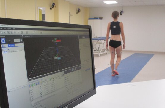 Kind mit Markern und Sensoren am Körper geht barfuß in Badebekleidung im klinischen Ganganalyselabor auf blauem Boden