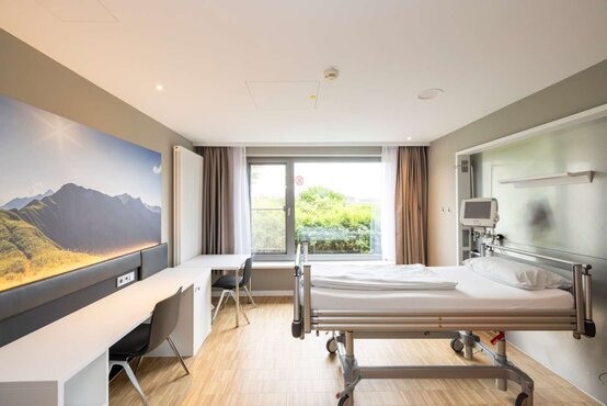 Modernes Wahlleistungszimmer mit Bett, Schreibtisch, großem Fenster, Holzfußboden und TV in der Schön Klinik Vogtareuth