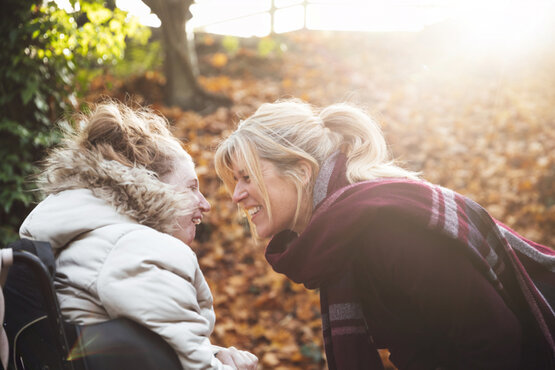 Lächelndes Kind im Rollstuhl und Frau draußen im Herbst