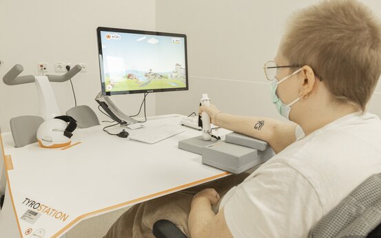 Patient trainiert Handmotorik mit Tyrostation-Eingabegerät vor Bildschirm im hellen Therapieraum