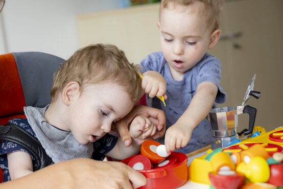 Zwei Kleinkinder spielen gemeinsam mit Spielküche im Spielzimmer