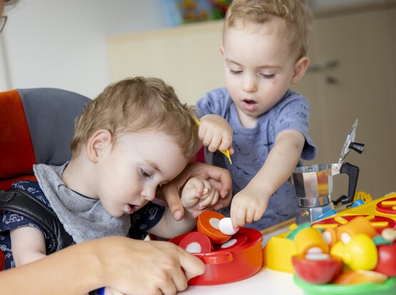 Zwei Kleinkinder spielen gemeinsam mit Spielküche im Spielzimmer