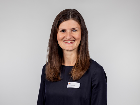 Julia Rößner, lächelt freundlich mit Namensschild im dunkelblauen Oberteil vor neutralgrauem Hintergrund im Klinik-Porträt