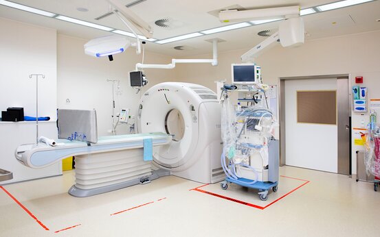 Moderner Klinikraum mit Computertomograph, CT-Liege, Überwachungsmonitor und weitere medizinische Geräte