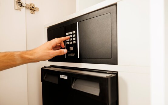 Hand gibt Zahlencode am Safe ein, Safe im weißen Einbauschrank eines modernen Patientenzimmers der Schön Klinik Vogtareuth