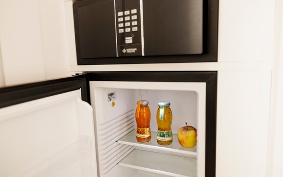 Offener Minikühlschrank und Safe im weißen Einbauschrank, zwei Flaschen Saft und Apfel auf mittlerer Glasablage