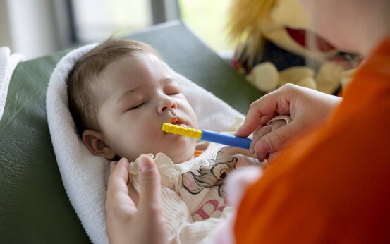 Therapeutin und Kleinkind gemeinsam bei Logopädie Übung mit blau-gelbem Stab