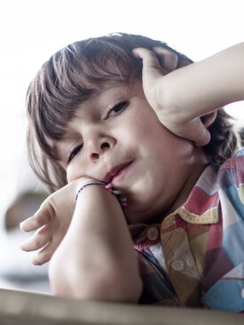 Kind in buntem Hemd sitzt am Tisch und hat die Hände am Kopf