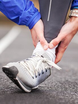 Person hält sich das umgeknickte Sprunggelenk