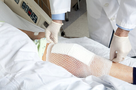 Arzt versorgt das bandagierte Bein eines Patienten mit chronischer Wunde im Krankenhausbett