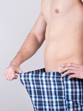 Mann blickt in heruntergezogene Boxershorts, Symbolbild für erektile Dysfunktion.