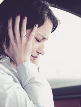 Junge Frau sitzt gestresst im Auto und hält sich die Ohren, leidet unter starker Geräuschempfindlichkeit