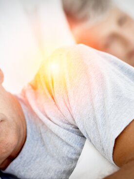 Nahaufnahme von zwei älteren Personen mit grauen Haaren, die nebeneinander im Bett schlafen, vorn Mann Fokus auf Schulter