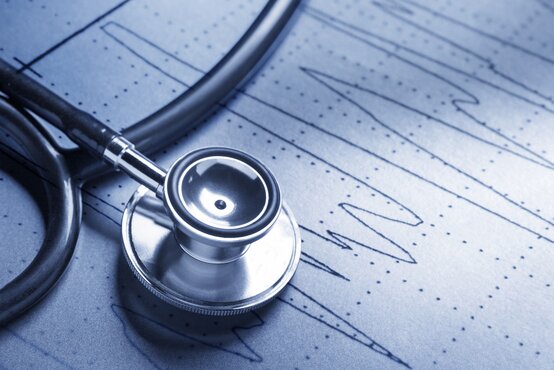 Stethoskop liegt auf EKG-Diagramm mit Kurvenlinien, Nahaufnahme in bläulichem Licht
