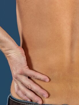 Rückenansicht eines unbekleideten Rückens vor blauem Hintergrund, zwei Hände umfassen die Taille, Fokus auf unteren Rücken