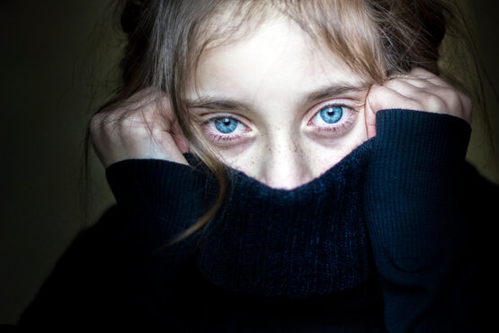 Kind mit hellbraunen Haaren zieht angespannt den Pullover am Gesicht hoch