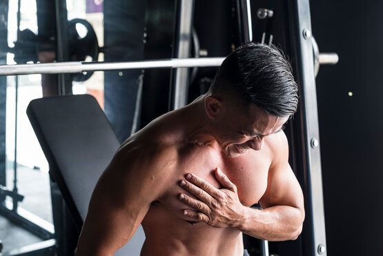 Muskulöser Mann hält sich schmerzhaft die Brust nach Verletzung beim Bankdrücken im Fitnessstudio