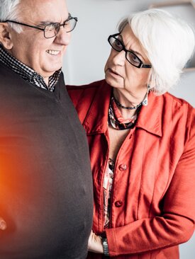 Älterer Mann hält sich schmerzverzerrt den Rücken, ältere Frau stützt ihn dabei