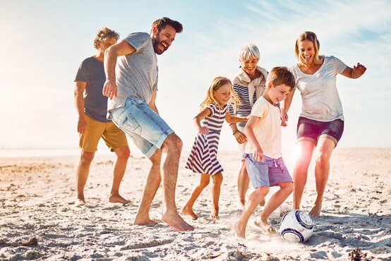 Familie spielt barfuß am sonnigen Strand Fußball, zeigt schmerzfreie Mobilität und Freude an Bewegung