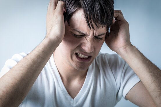 Mann hält sich mit beiden Händen am Kopf, schaut dabei angestrengt