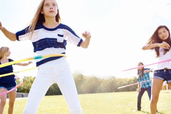 Jugendliche trainieren bei Sonnenschein auf grüner Wiese mit bunten Hula-Hoop-Reifen, Fokus auf Beweglichkeit und Koordination