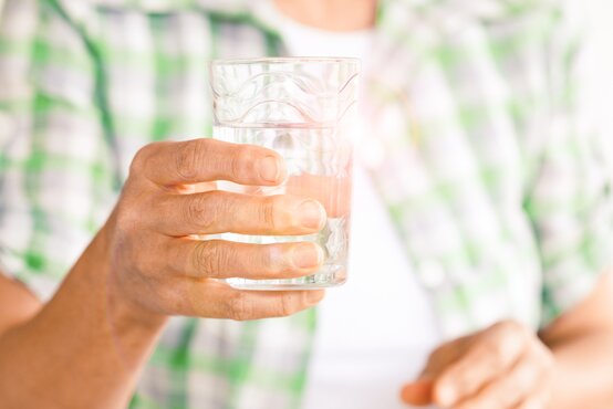 Person in grün-weißem Hemd hält in einer Hand ein Wasserglas