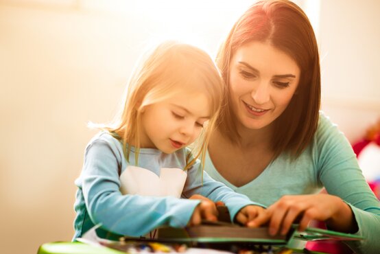 Erwachsene Sprachtherapeutin und Mädchen lesen konzentriert in therapeutischem Buch