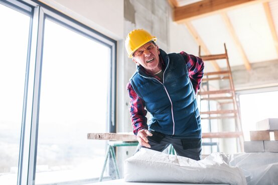 Bauarbeiter mit Schutzhelm hält sich schmerzhaft den Rücken im Rohbau