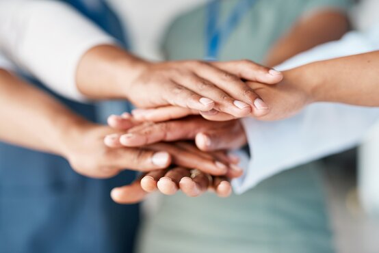 Mehrere verschiedene Hände liegen übereinander – Symbol für Teamwork, Vielfalt und Zusammenarbeit im beruflichen Umfeld