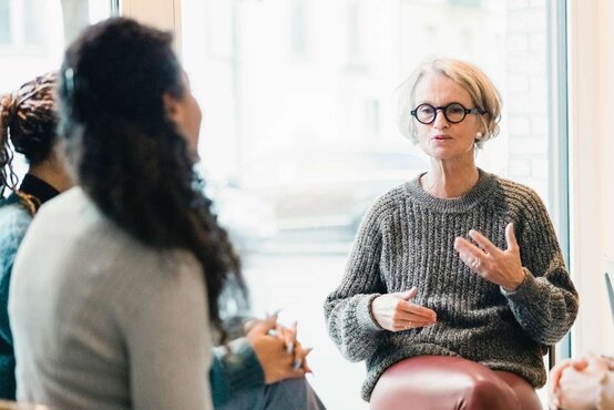 Frau leitet Gruppentherapie für Demenz in hellem Raum, Gesprächsgruppe im Vordergrund