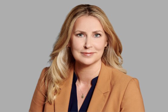 Kathy Döhler. Porträt einer blonden Frau mit langen, gewellten Haaren im hellbraunen Blazer und dunkelblauer Bluse