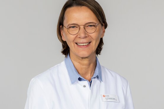 Elisabeth Rauh. Porträt einer Ärztin mit runder Brille und kurzem braunem Haar im weißen Kittel