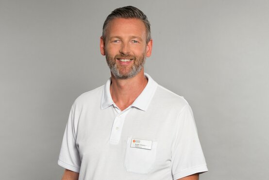 Dr. Johannes Sander. Porträt eines freundlichen Arztes in weißer Klinikkleidung mit Namensschild