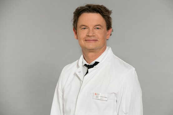 Dr. Ralph Kothe. Porträt eines Mannes mit kurzen, braunen Haaren im weißen Arztkittel und Namensschild