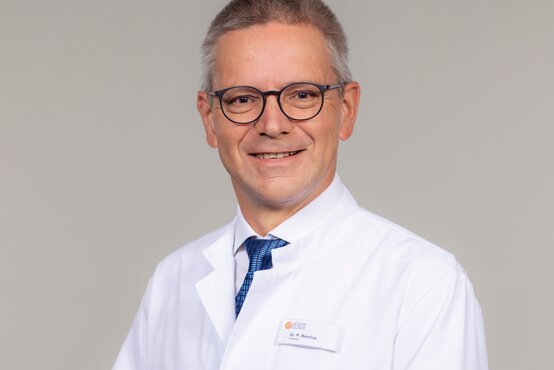 Dr. Peter Bernius, Orthopäde der Schön Klinik München Harlaching, im weißen Arztkittel vor neutralem Hintergrund