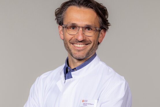 Prof. Dr. Kai Megerle, Chefarzt für Plastische Chirurgie an der Schön Klinik München Harlaching, vor hellem Hintergrund