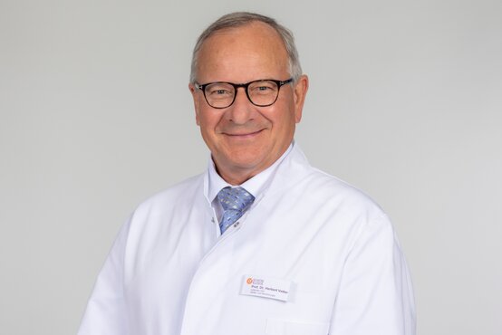Porträt von Prof. Dr. Herbert Vetter im weißen Arztkittel mit Namensschild und blauer Krawatte