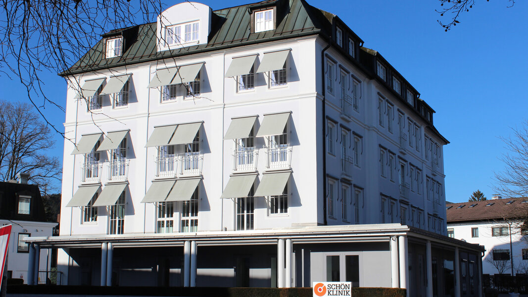 Mehrstöckiges, weißes Gebäude mit Markisen und Schön-Klinik-Logo bei blauem Himmel