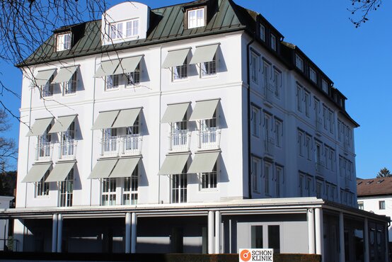 Mehrstöckiges, weißes Gebäude mit Markisen und Schön-Klinik-Logo bei blauem Himmel