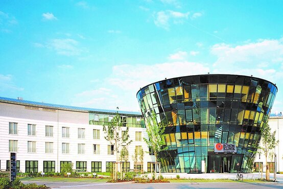 Modernes Gebäude der ehemaligen Schön Klinik Nürnberg Fürth mit gläsernem, trichterförmigem Eingangsbereich und weißem Flachbau