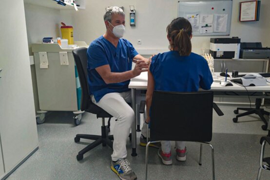 Arzt impft Patientin im Behandlungsraum einer Klinik