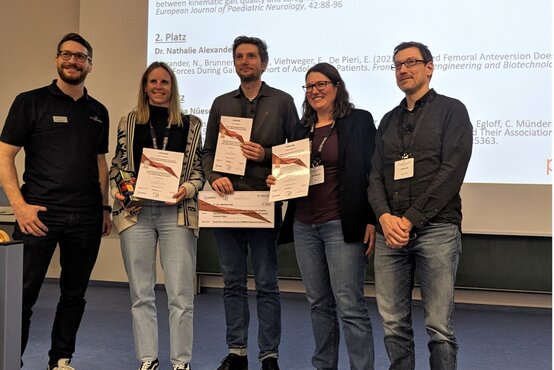 Personen mit Namensschildern erhalten auf Bühne Urkunden und Trophäe bei Preisverleihung, Präsentation mit Preisträgernamen im Hintergrund