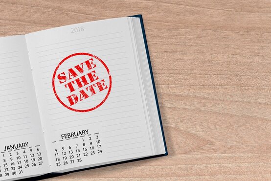 Offener Kalender 2018 auf Holztisch mit rotem „Save the Date“-Stempel