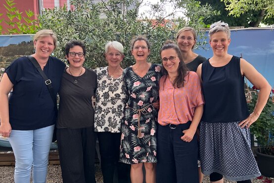 Sieben lachende Frauen des Teams Schön Klinik Vogtareuth stehen Arm in Arm vor Gebäude