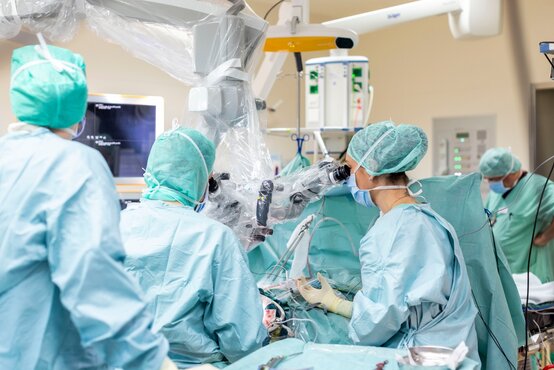 Chirurgen-Team in OP-Kleidung arbeitet konzentriert mit Mikroskop am Kopf eines Patienten, moderner Operationssaal mit medizinischer Technik