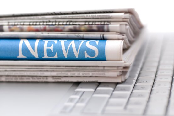 Stapel gefalteter Zeitungen auf Computertastatur, vorn Zeitung mit blauem Titelstreifen und weißem „NEWS“-Schriftzug